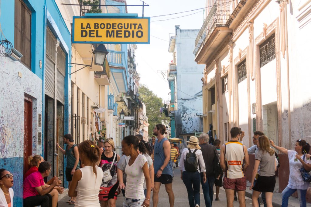 Amidst the historic Obispo street in Old Havana, Cuba, Bar La Bodeguita del Medio exudes timeless charm as tourists stroll beneath the sun's warm embrace, painting a quintessentially Cuban scene.