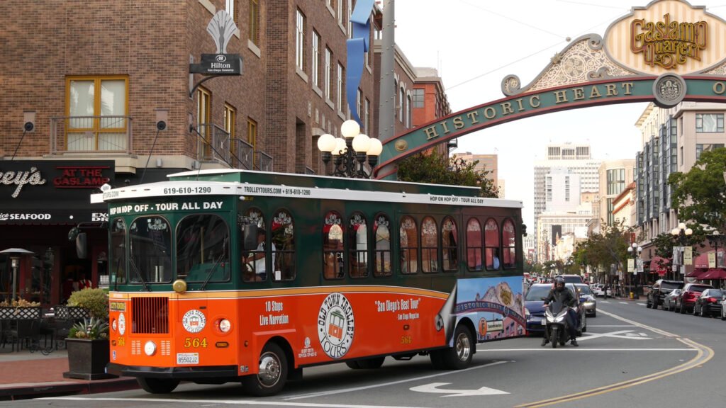 San Diego, California, USA, the historic entrance arch sign of the Gaslamp Quarter stands proudly on 5th Avenue, welcoming visitors. An iconic orange retro trolley and hop-on-hop-off bus highlight the area's charm, a must-see on the Old Town Sightseeing Tour.