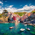Riomaggiore, the debut jewel in Cinque Terre's hill cities, bathed in dawn's glow. Pastel buildings cascade, framing a tranquil Mediterranean seascape. A captivating spring morning in Liguria, Italy.